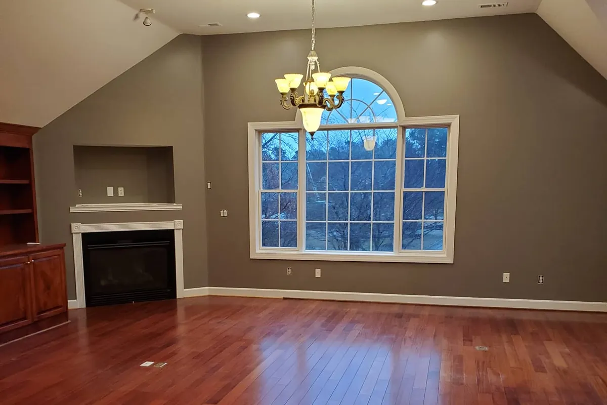 Empty great room with gray-green walls, white fireplace mantel, arched window and cherry hardwood floors