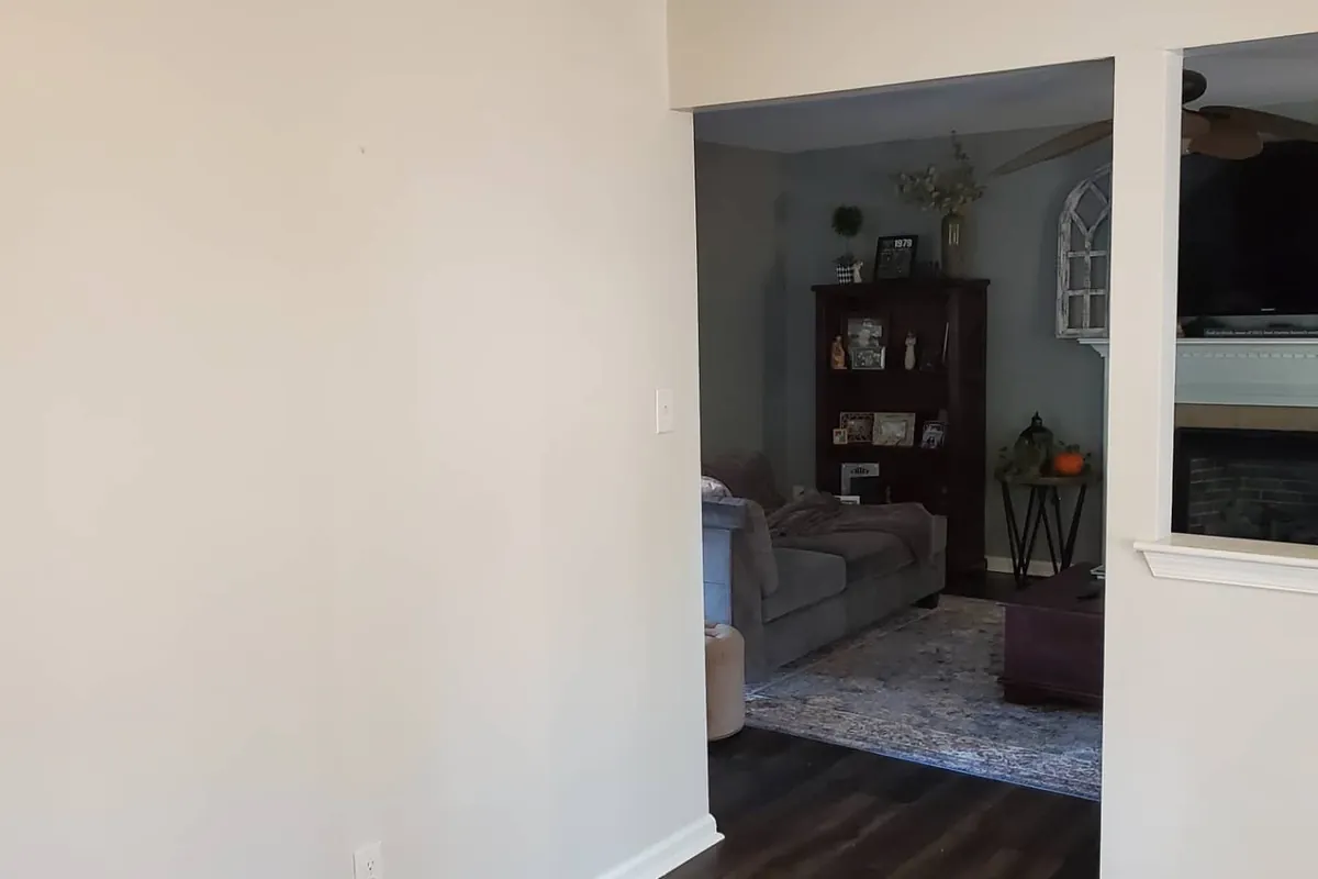 Greige dining room wall with white baseboard opening to gray living room and fireplace