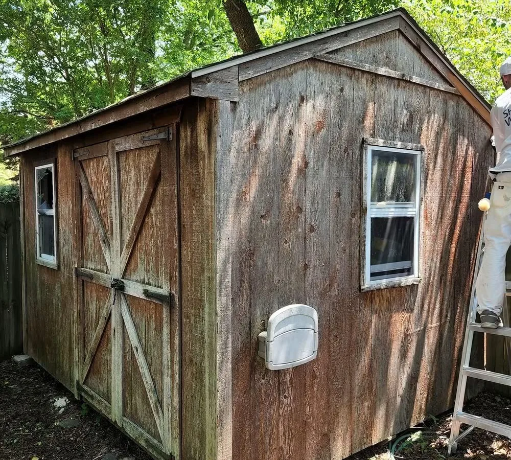 Garden shed before work, board-and-batten siding weathered gray and blotched where the old finish had gone