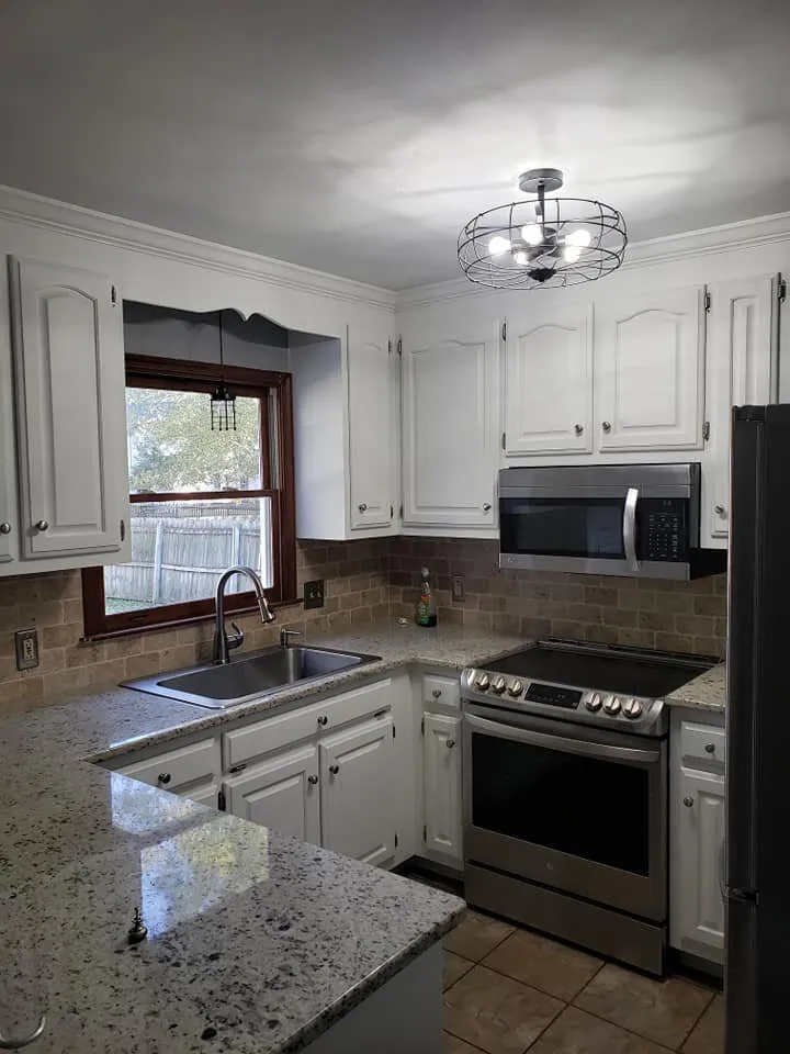Kitchen with cabinets refinished in white, granite counters, stone tile backsplash and stainless appliances