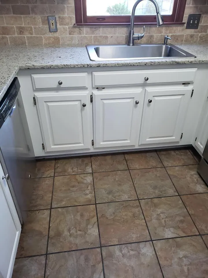 Refinished white kitchen base cabinets under granite counter with stainless sink and tile floor