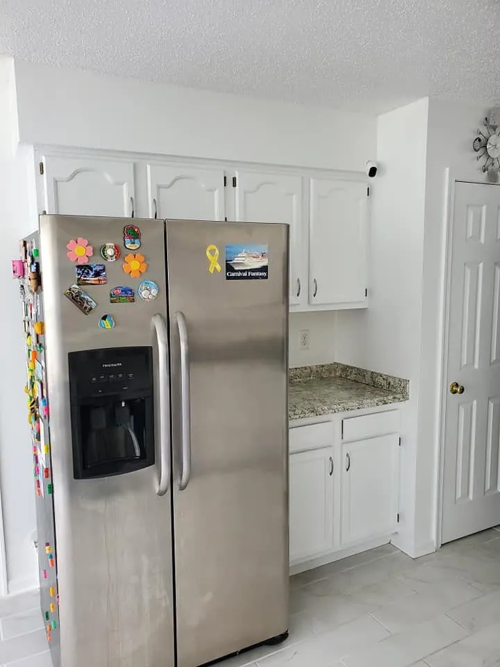 Kitchen corner with white painted cabinets, granite counter, stainless refrigerator and white six-panel door