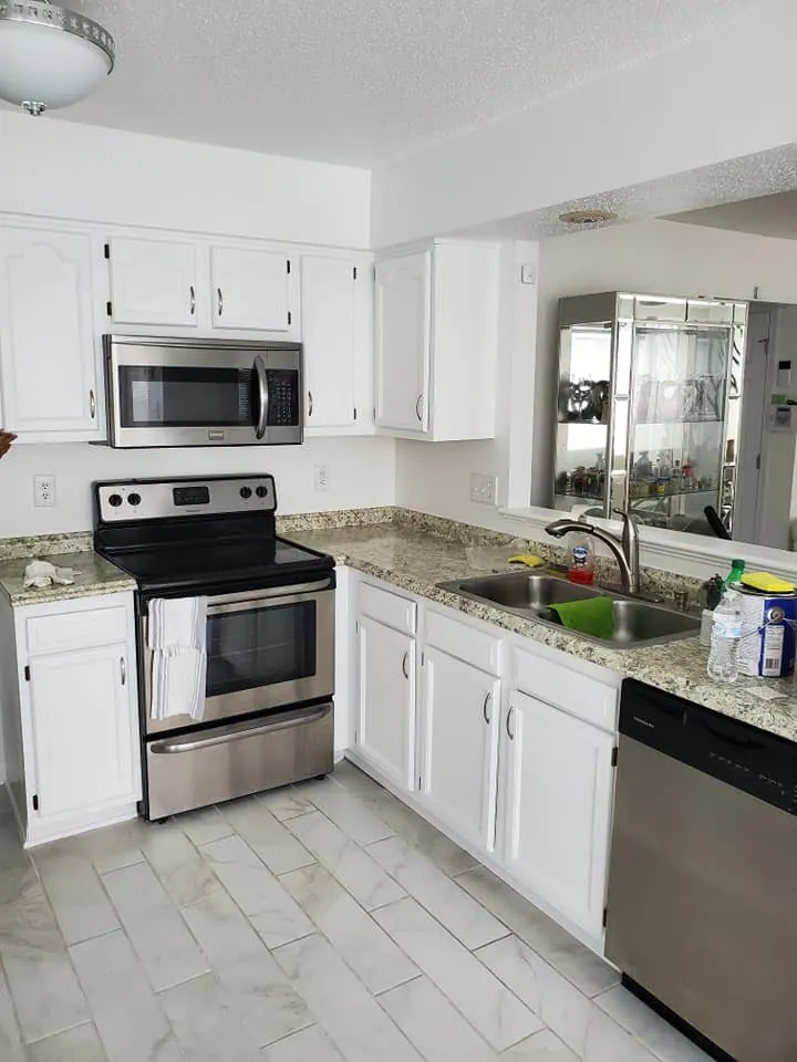 Kitchen with cabinets refinished white, granite counters, stainless appliances and marble-look tile floor