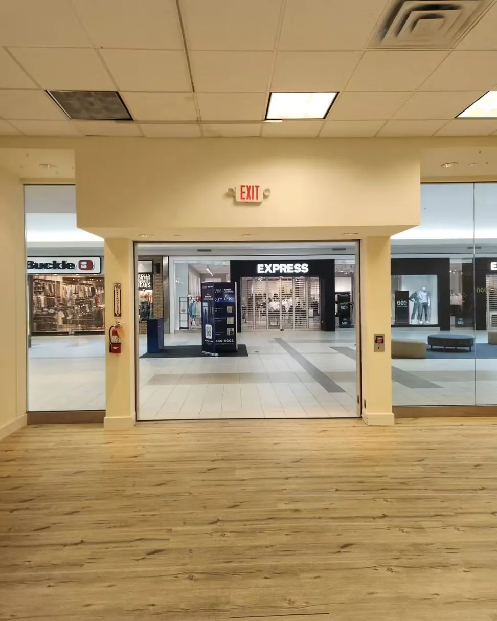 Mall retail unit after repainting, the bulkhead and columns in warm cream, cut in around a live exit sign and the neighboring shopfronts