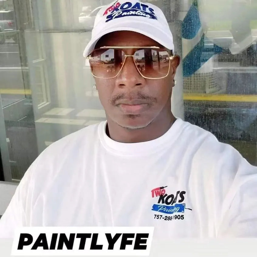 Two Koats Painting crew member in a branded cap and work shirt carrying the company phone number