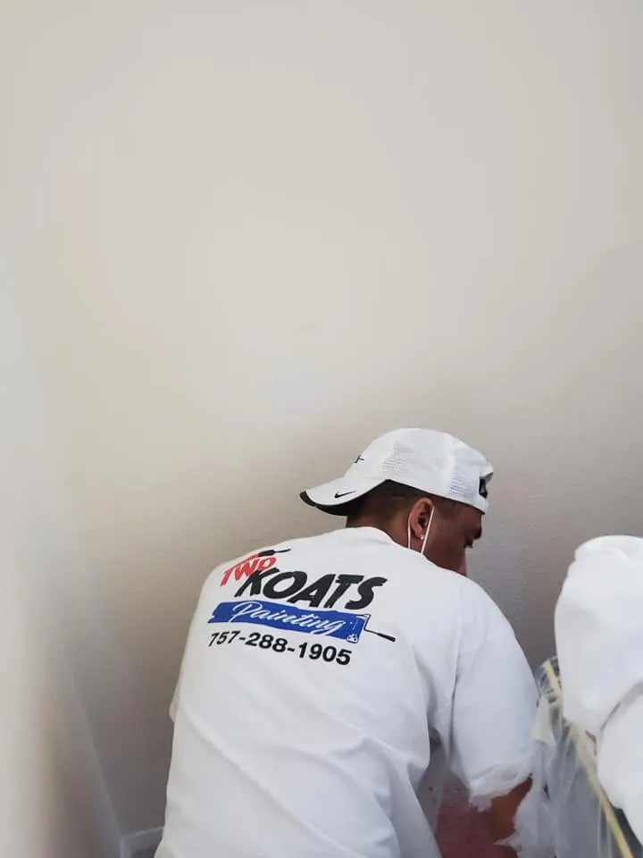 Painter wearing a Two Koats Painting shirt with phone number working at a white wall corner