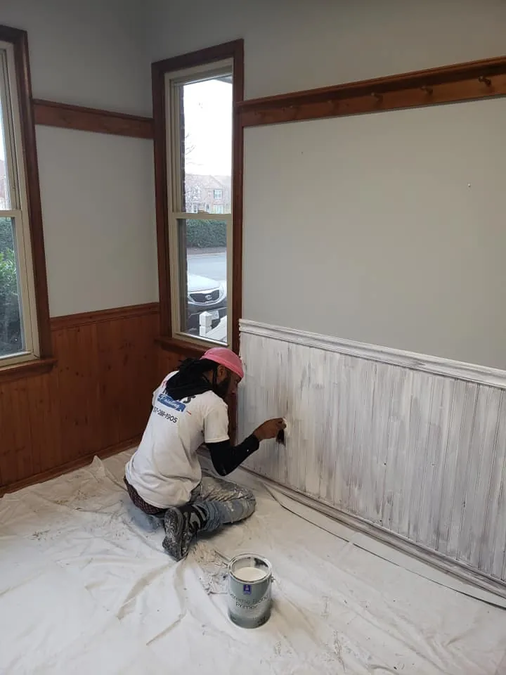 Painter in Two Koats branded shirt brushing white primer onto wood beadboard wainscoting