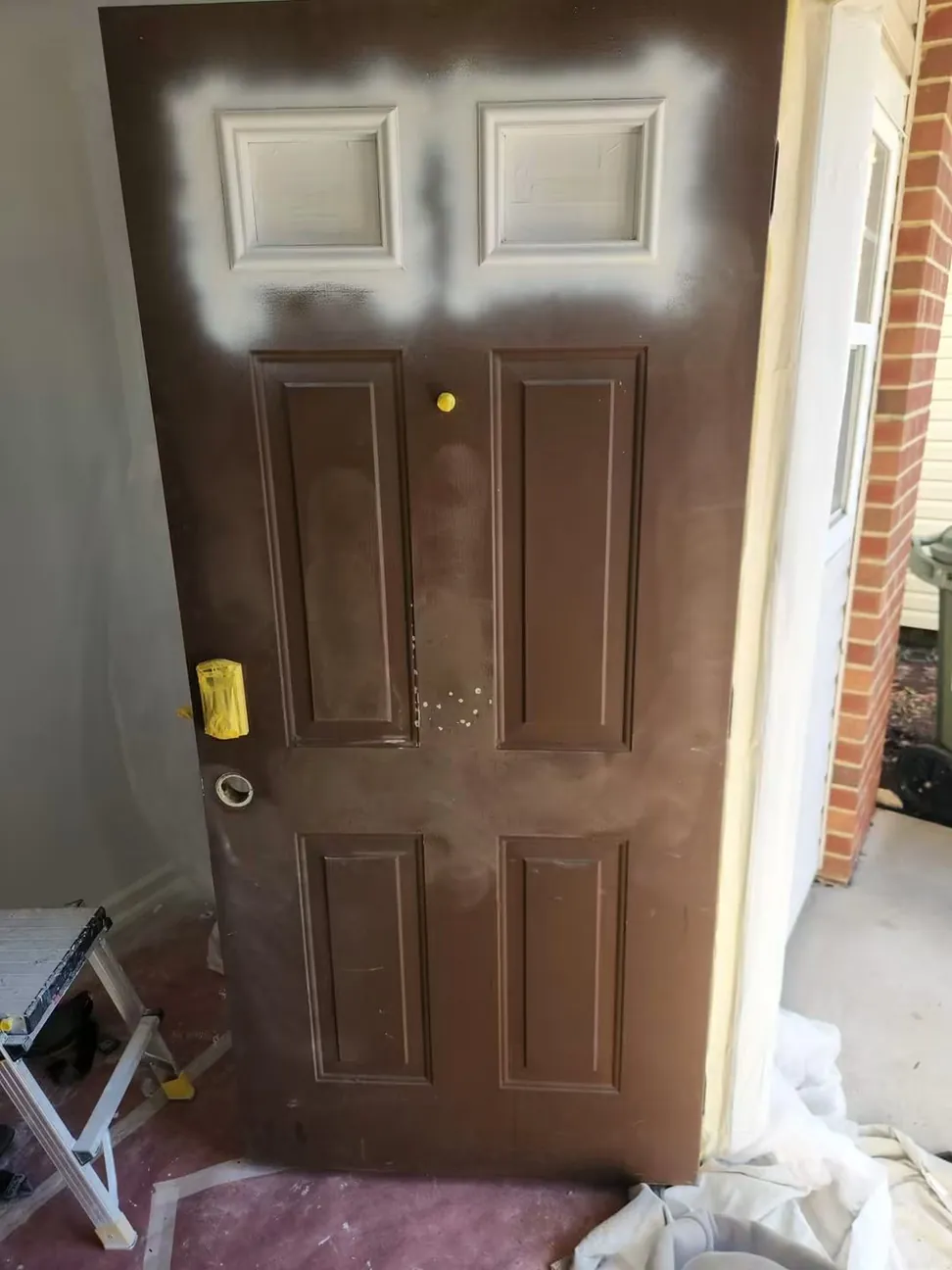 The same front door before finishing, old brown coating spot-primed at the top rail with the floor papered off