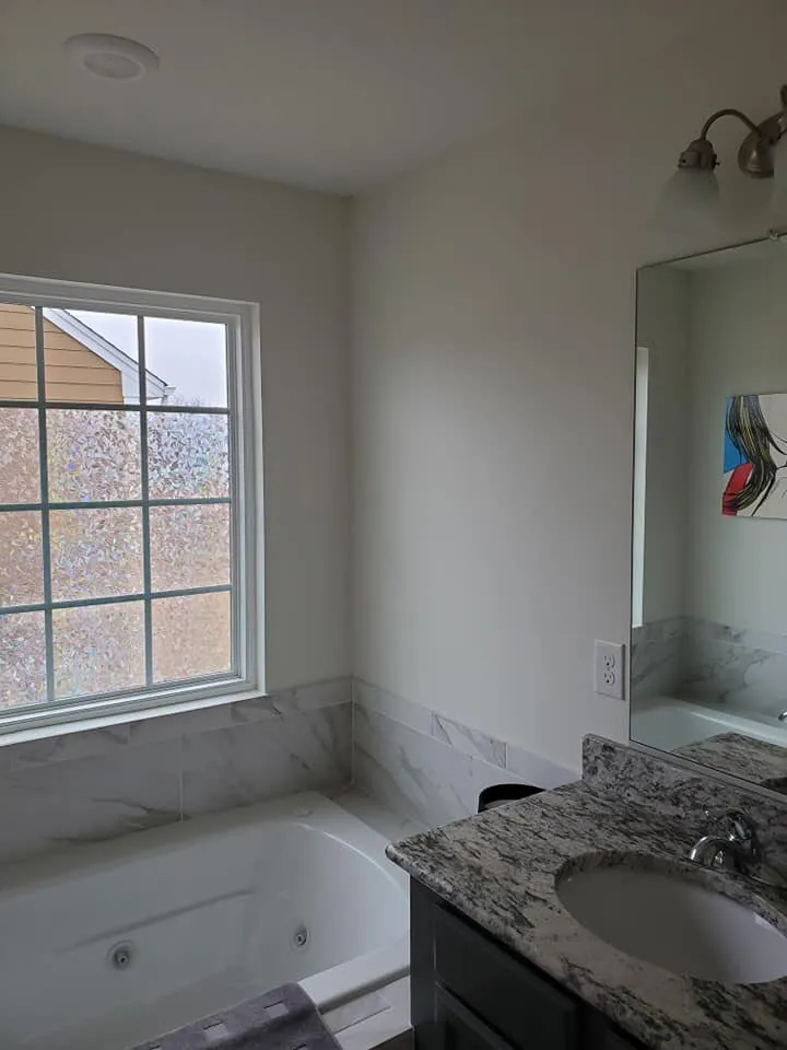 Bathroom with white walls, marble tile tub surround, soaking tub and granite vanity top