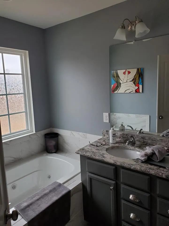 Bathroom painted blue-gray with corner jetted tub, marble tile surround and dark gray granite-topped vanity