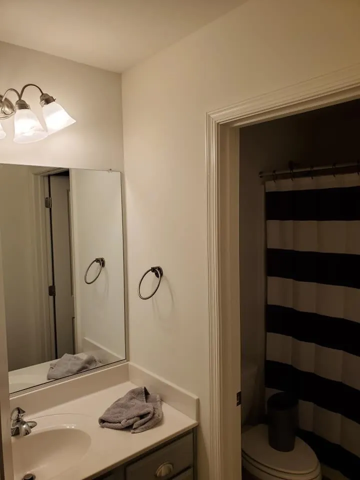 Bathroom with cream walls, mirror and gray vanity beside doorway to striped shower curtain