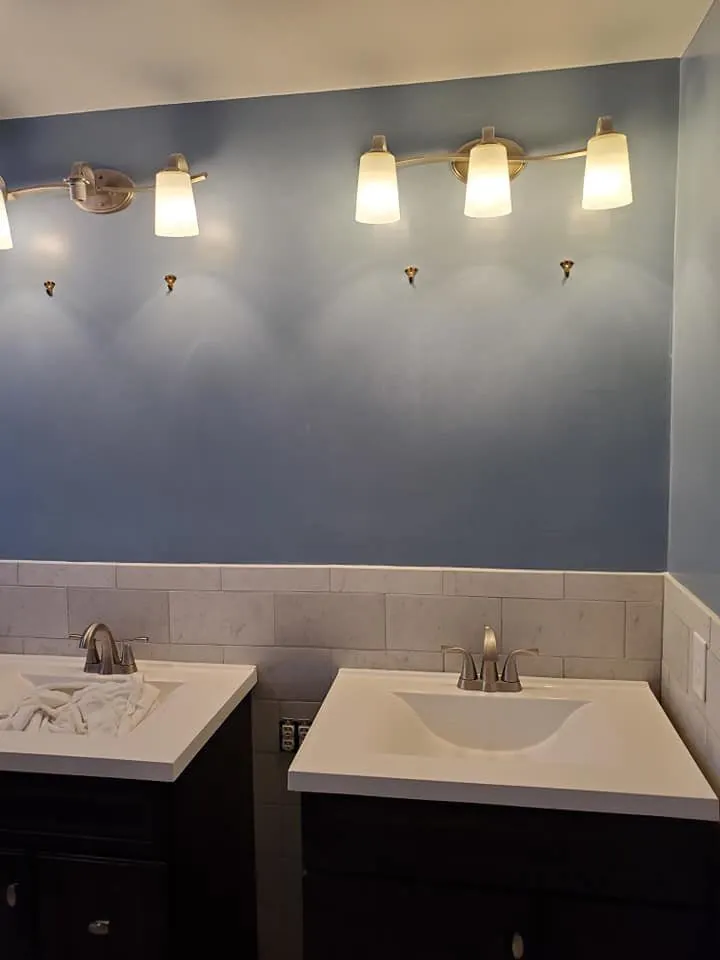 Bathroom with two dark vanities, white sinks, blue painted wall, and marble subway tile