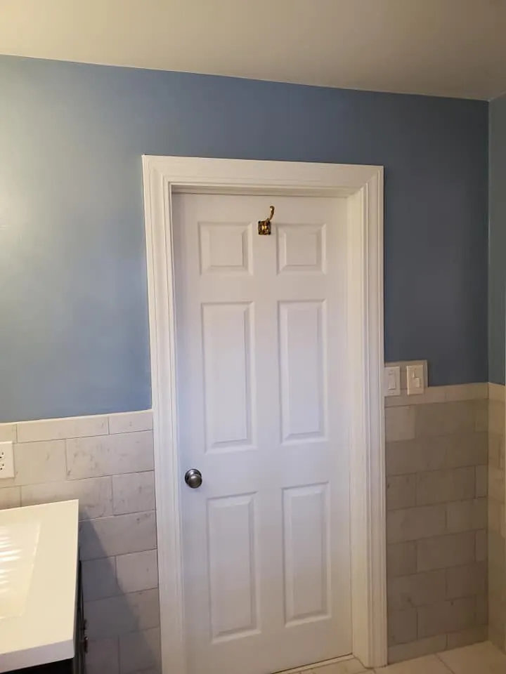 Bathroom with medium blue walls, white six-panel door and trim above marble subway tile wainscot