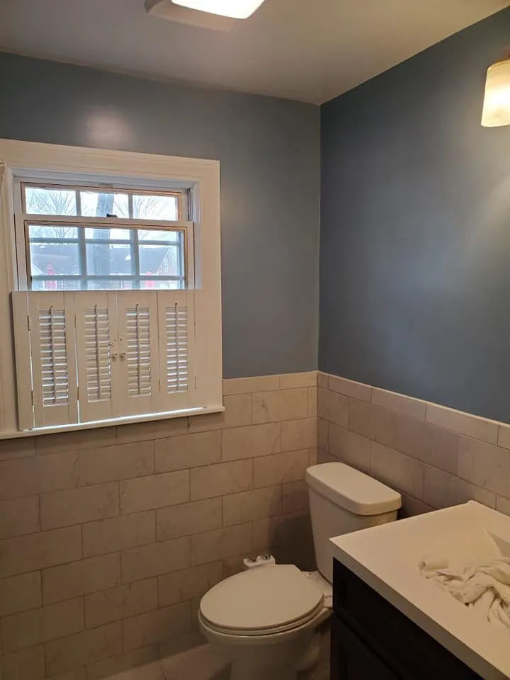 Bathroom painted slate blue above marble tile wainscot with white toilet and dark vanity