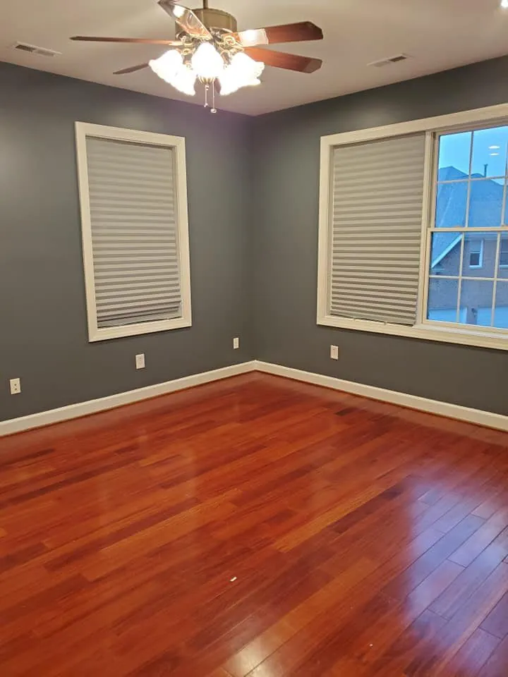 Empty bedroom with slate gray walls, white baseboards, cherry hardwood floor and ceiling fan