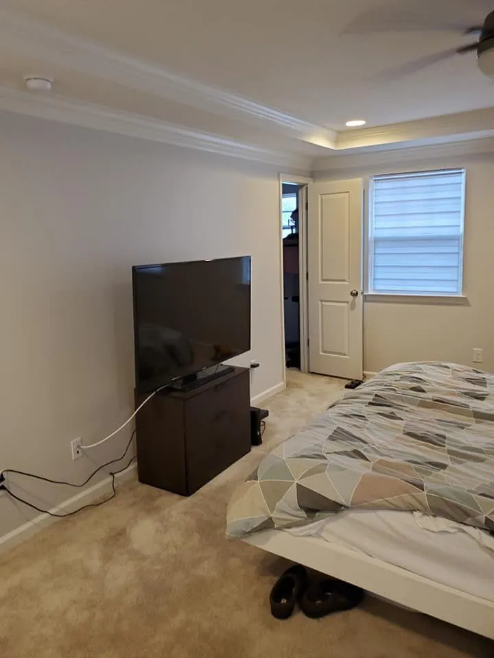 Bedroom with light greige walls, crown molding tray ceiling, flat screen TV on dresser and bed
