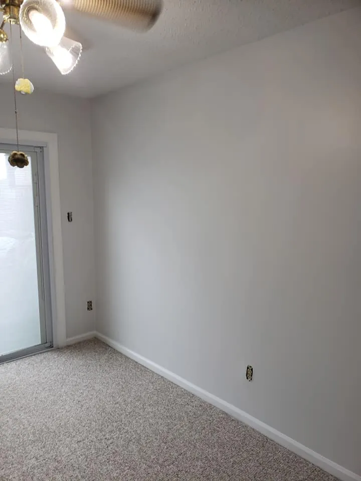 Empty bedroom with light gray walls, white baseboards, beige carpet and sliding glass door