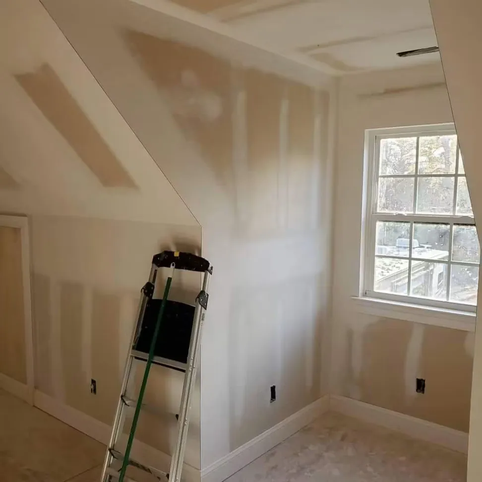 The dormer bedroom at drywall stage, joints taped and sanded under the sloped ceiling before any paint