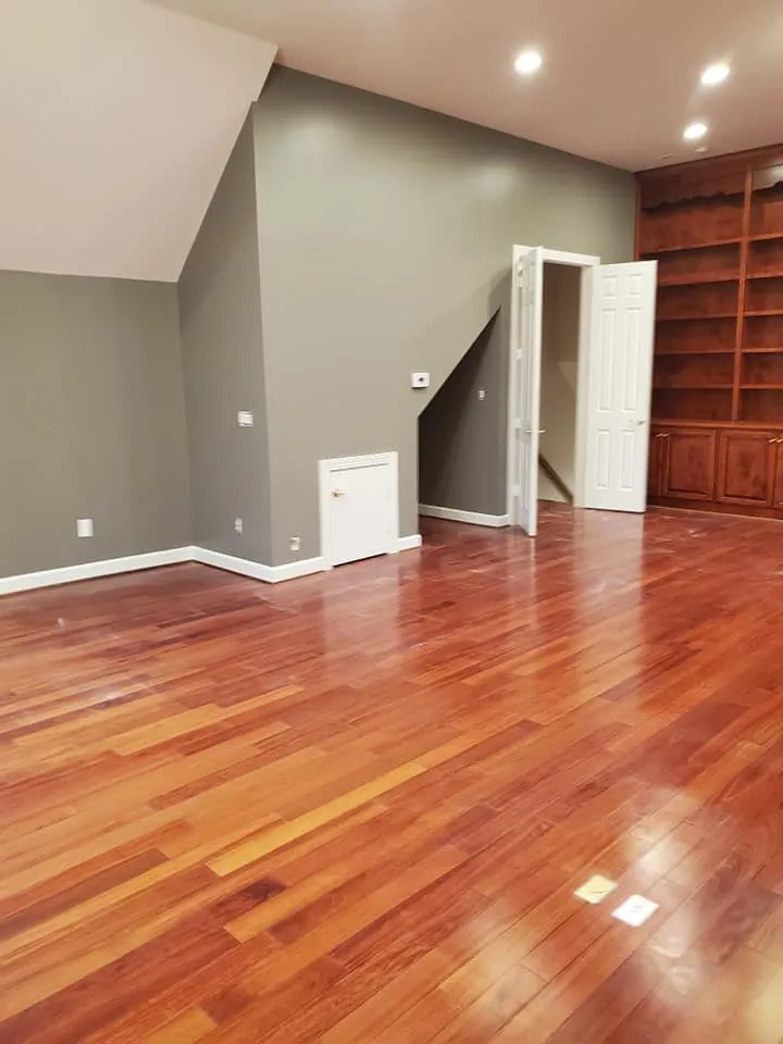 Room painted sage gray with white trim, cherry hardwood floor and dark built-in bookshelves