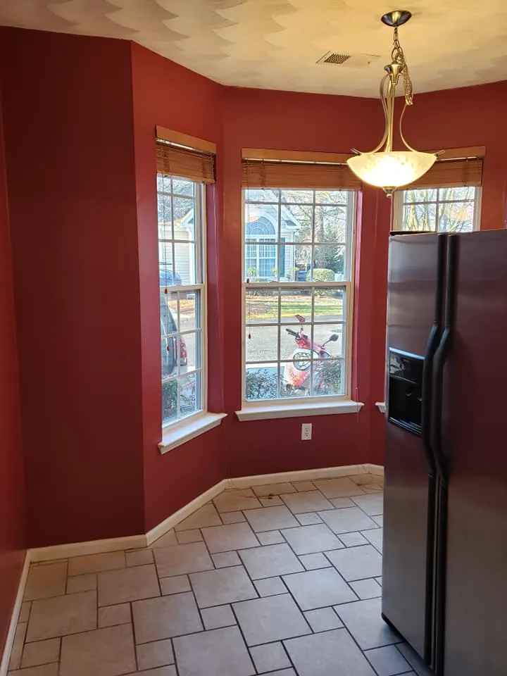 Kitchen breakfast nook painted deep red with bay windows, white trim and beige tile floor