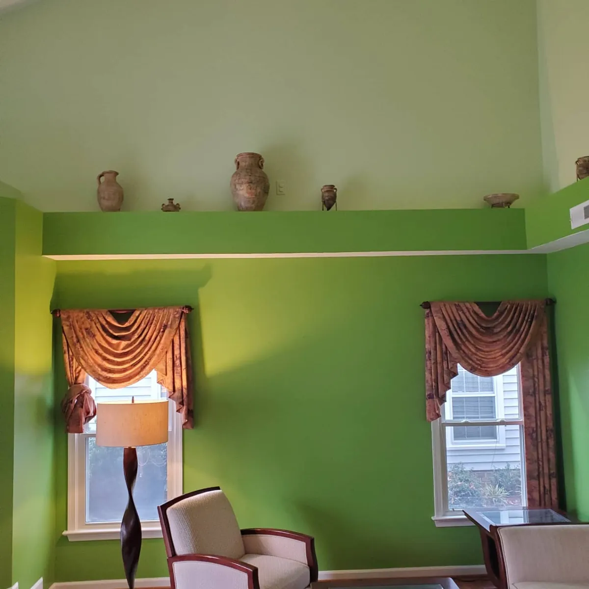 Sitting room with bright green walls, cream vaulted ceiling, pottery on ledge, and draped windows