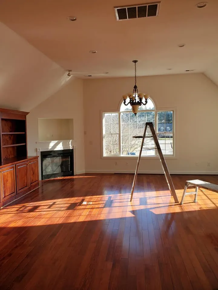 Vaulted great room with cream walls, arched window, iron chandelier, fireplace and cherry hardwood floor