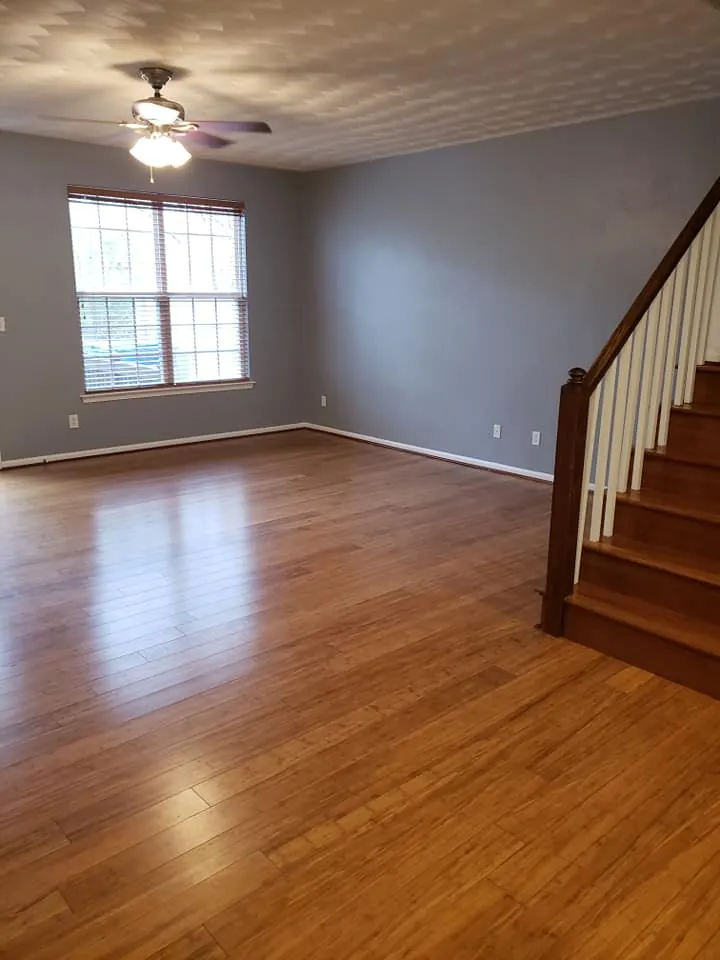 Empty living room with blue-gray walls, white trim, bamboo flooring and wood staircase