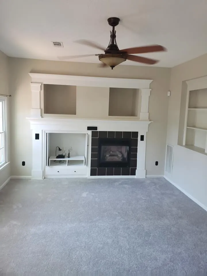 Empty living room with white painted fireplace mantel, built-in shelving and tan walls