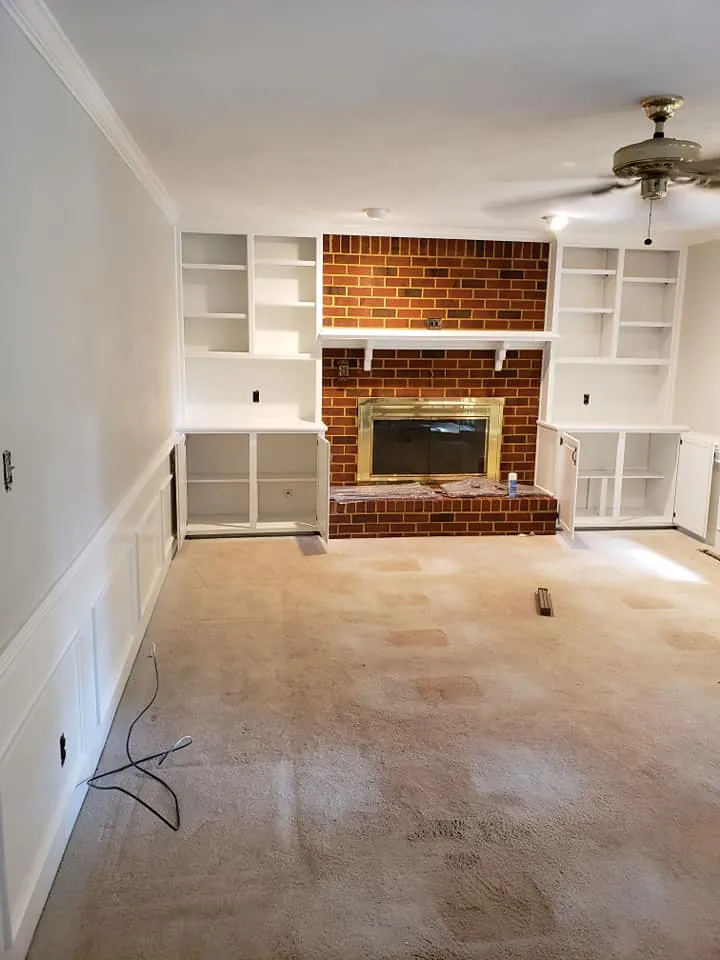Empty living room with white painted built-in shelves and wainscoting flanking a red brick fireplace