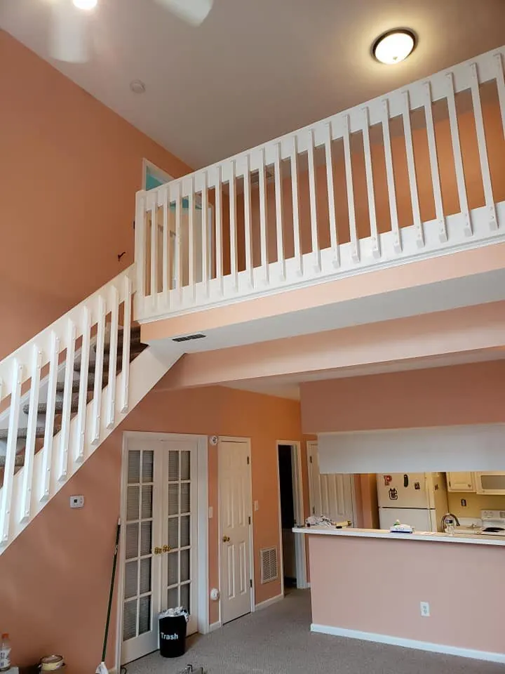 Two-story great room with salmon walls, white loft railing and staircase balusters above a kitchen pass-through