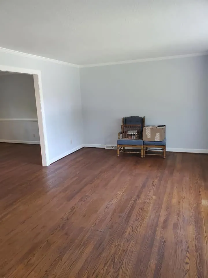 Empty living room with light gray walls, white crown molding and dark hardwood floors