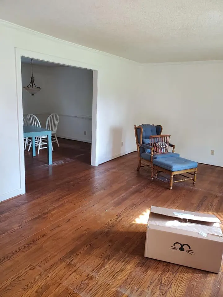 Living room with white walls and hardwood floor opening to a dining room with table
