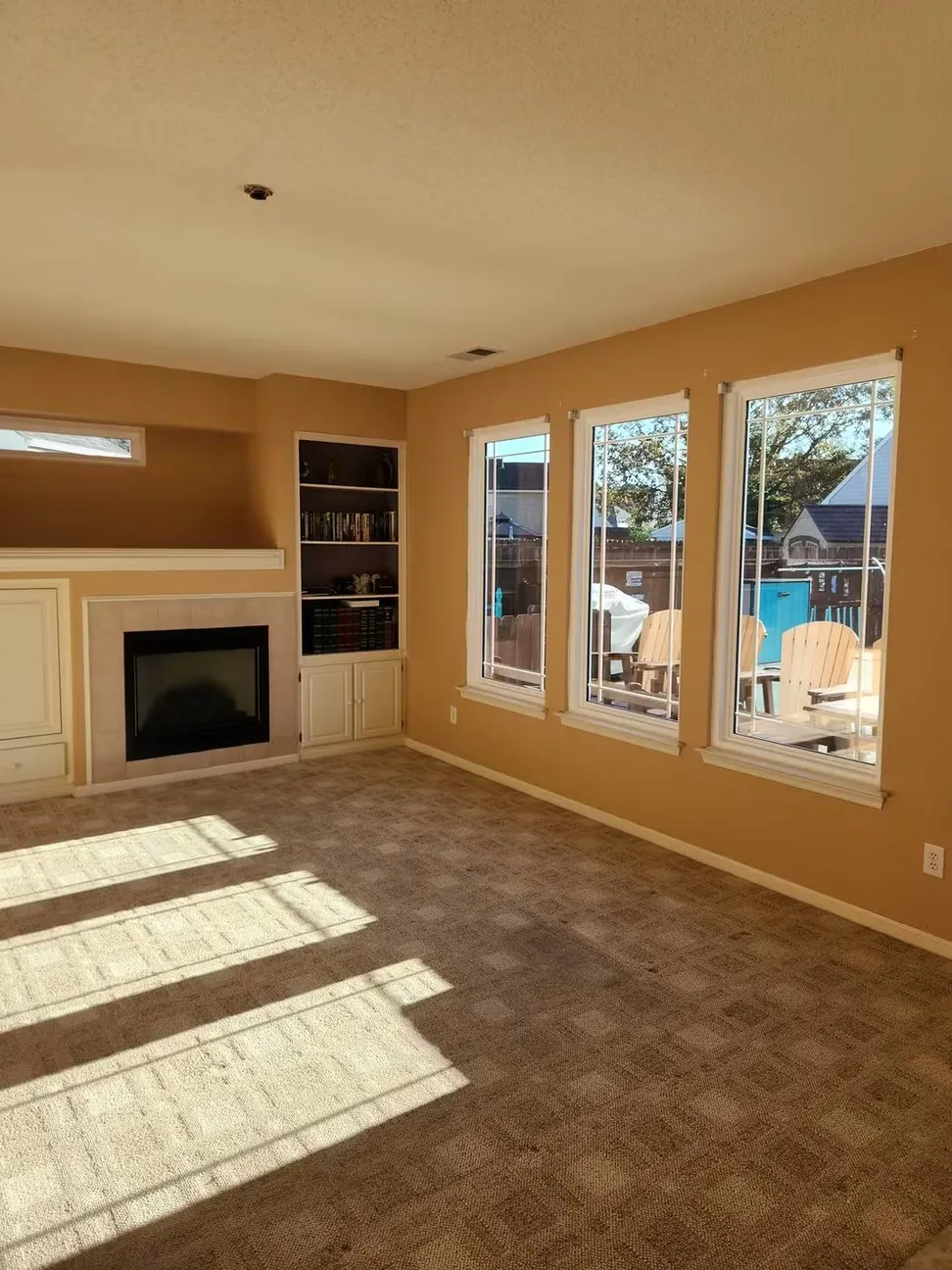 The same living room before work, tan walls from the fireplace end with the run of three windows and the built-in shelving