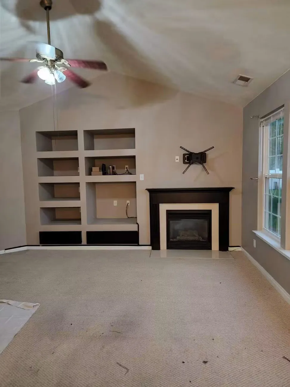 The same great room before work, beige throughout with a dark wood fire surround