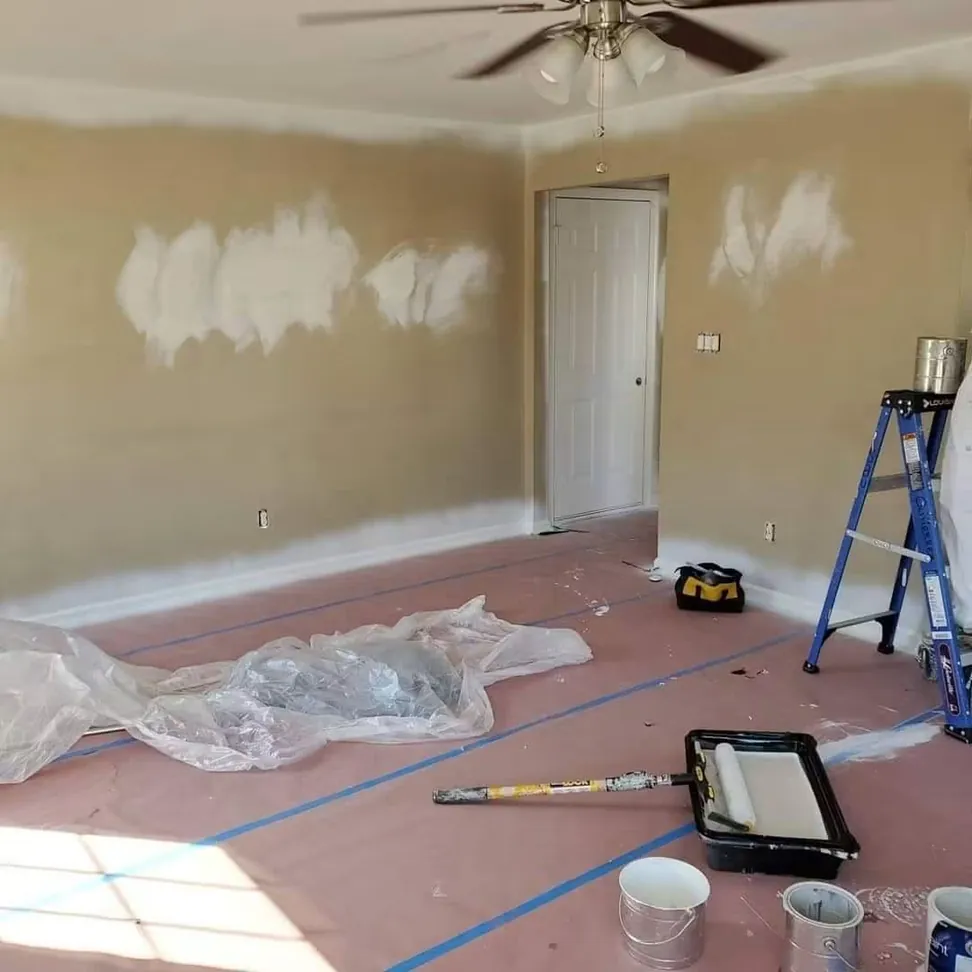 The same living room mid-job, filler patches drying across the wall and the floor papered and taped