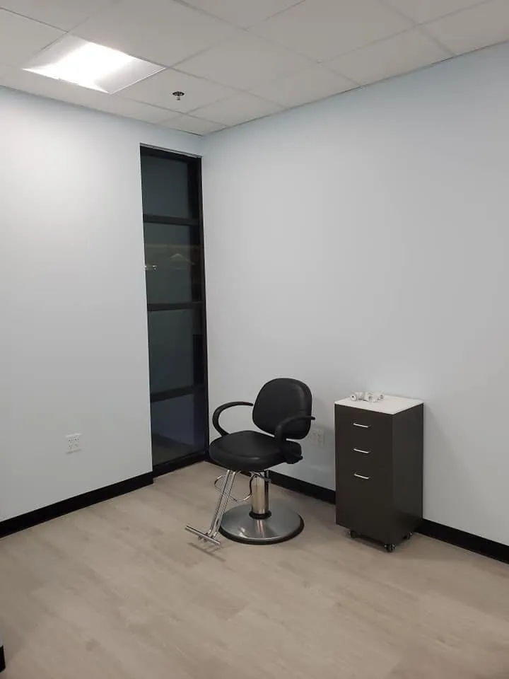 Small salon room with white walls, black baseboard, styling chair, and light wood flooring