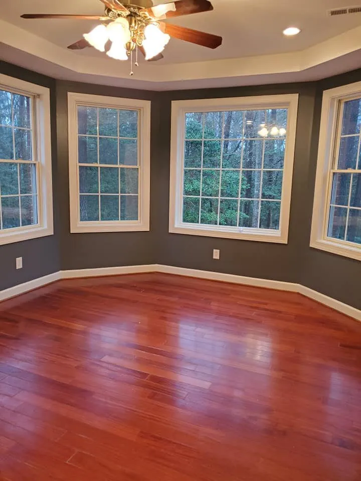 Empty room with charcoal gray walls, white window trim, bay windows and glossy cherry hardwood floor