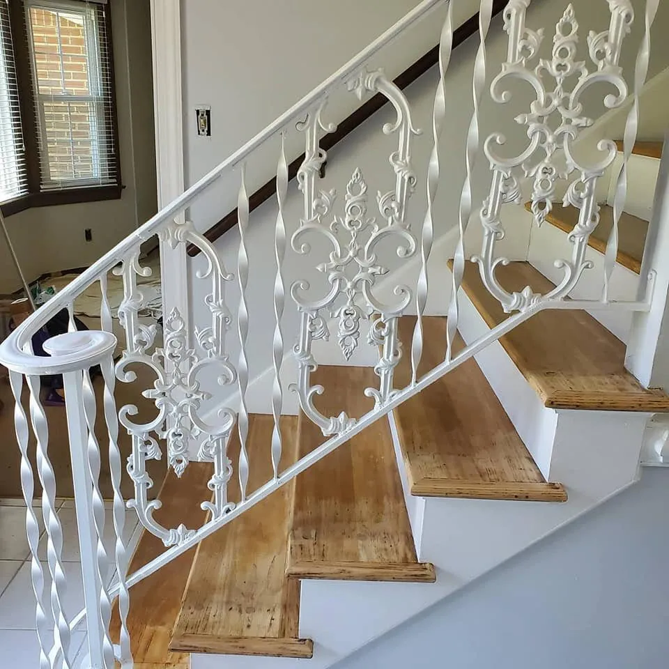 Ornate white-painted iron stair railing with scrollwork panels above bare wood stair treads