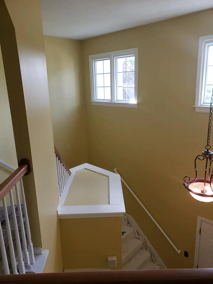 Stairwell landing painted gold with white balusters, handrail and window trim above carpeted stairs
