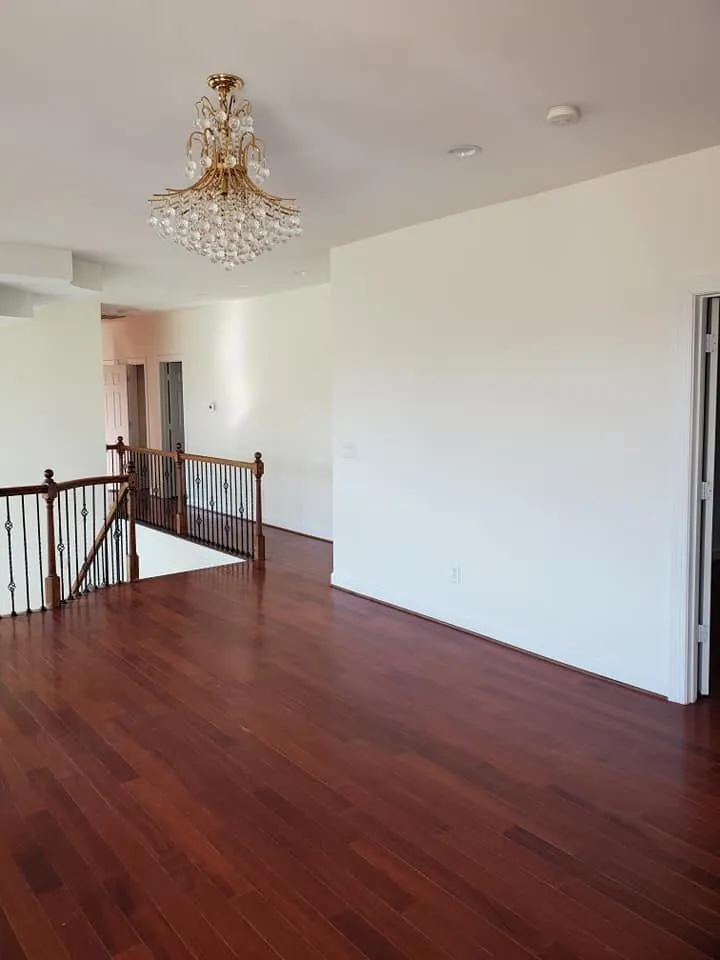 Empty upstairs landing with white walls, cherry hardwood floors, crystal chandelier, and iron balustrade